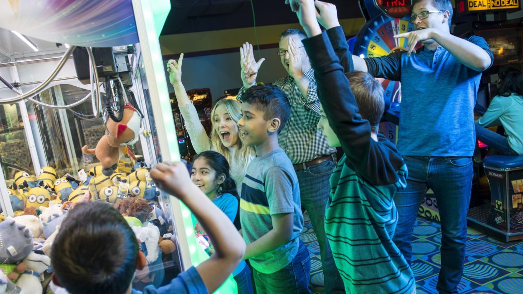 kids playing claw machine while kids spectate