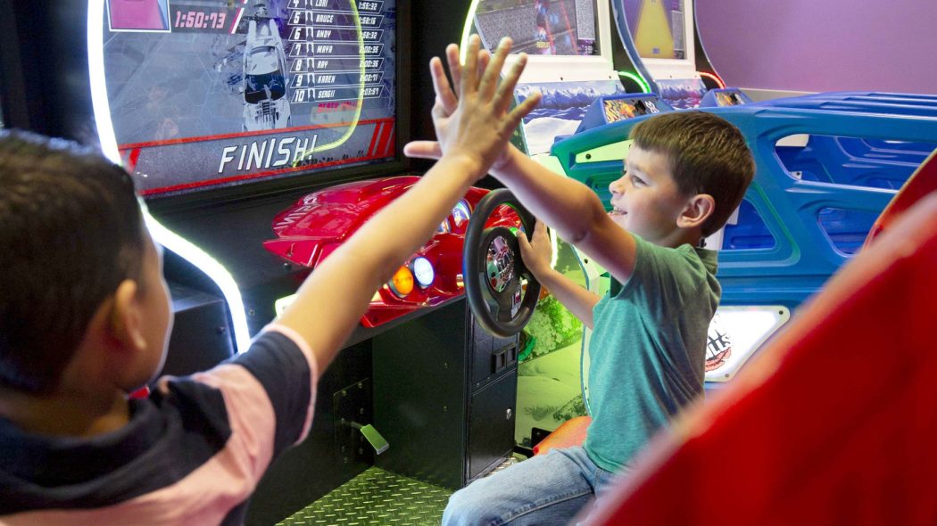 Kids high fiving while playing boat racing arcade game.